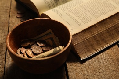 Photo of Donate and give concept. Bowl with coins, dollar banknotes and Bible on wooden table, closeup