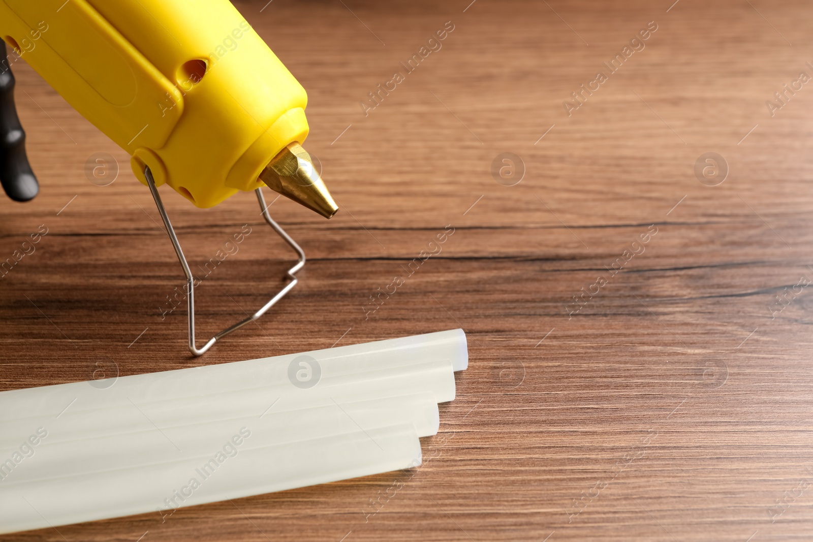 Photo of Yellow glue gun and sticks on wooden table, closeup. Space for text