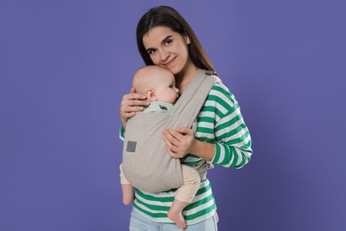 Mother holding her child in sling (baby carrier) on purple background