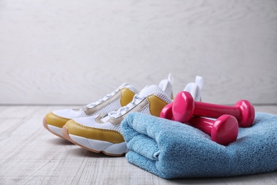 Photo of Dumbbells, sneakers and towel on floor, space for text. Home fitness