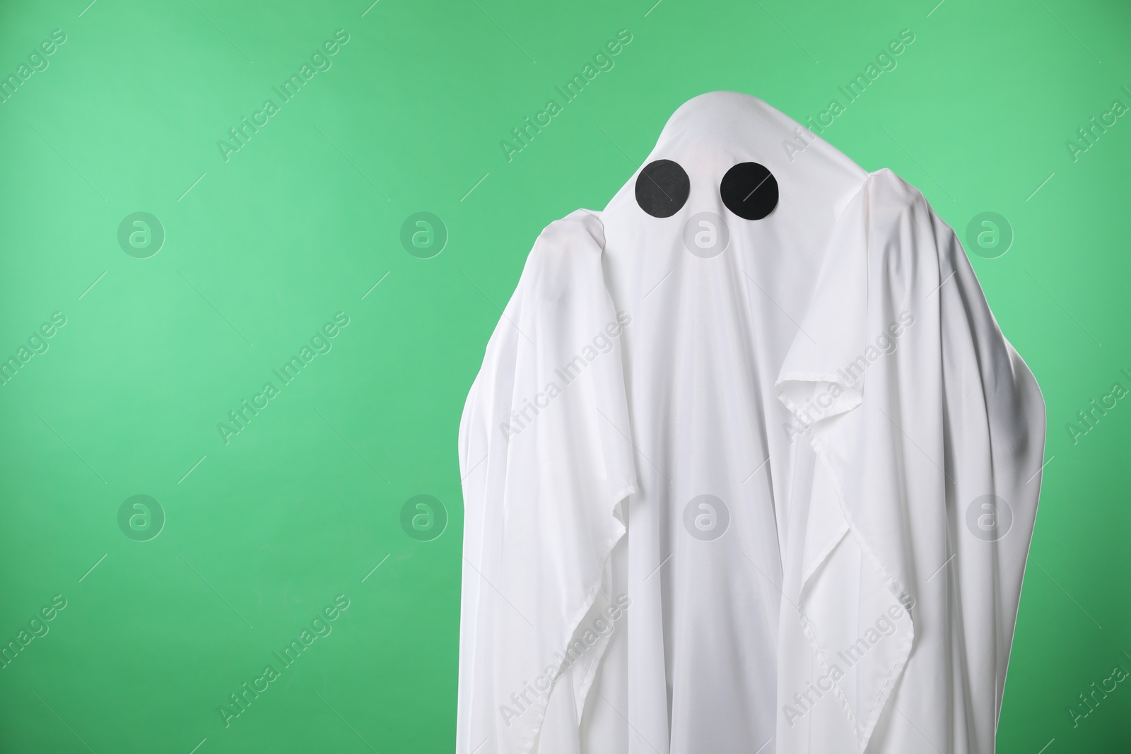 Photo of Creepy ghost. Person covered with white sheet on green background, space for text