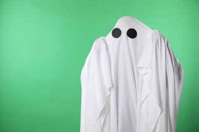 Creepy ghost. Person covered with white sheet on green background, space for text