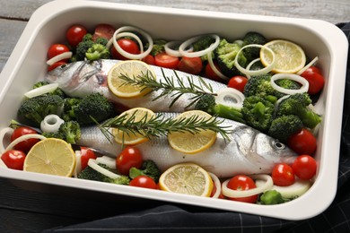 Photo of Raw fish with vegetables and lemon in baking dish on table