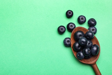 Photo of Fresh acai berries with wooden spoon on green background, flat lay. Space for text