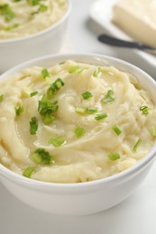 Photo of Bowl of delicious mashed potato with green onion on white table, closeup