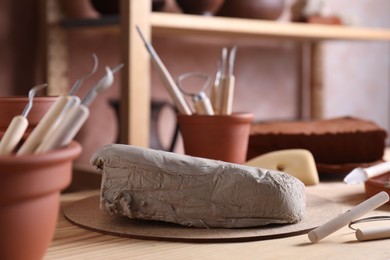 Photo of Clay and set of modeling tools on wooden table in workshop, closeup