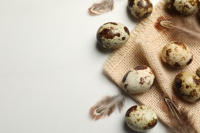 Photo of Speckled quail eggs and feathers on white table, flat lay. Space for text