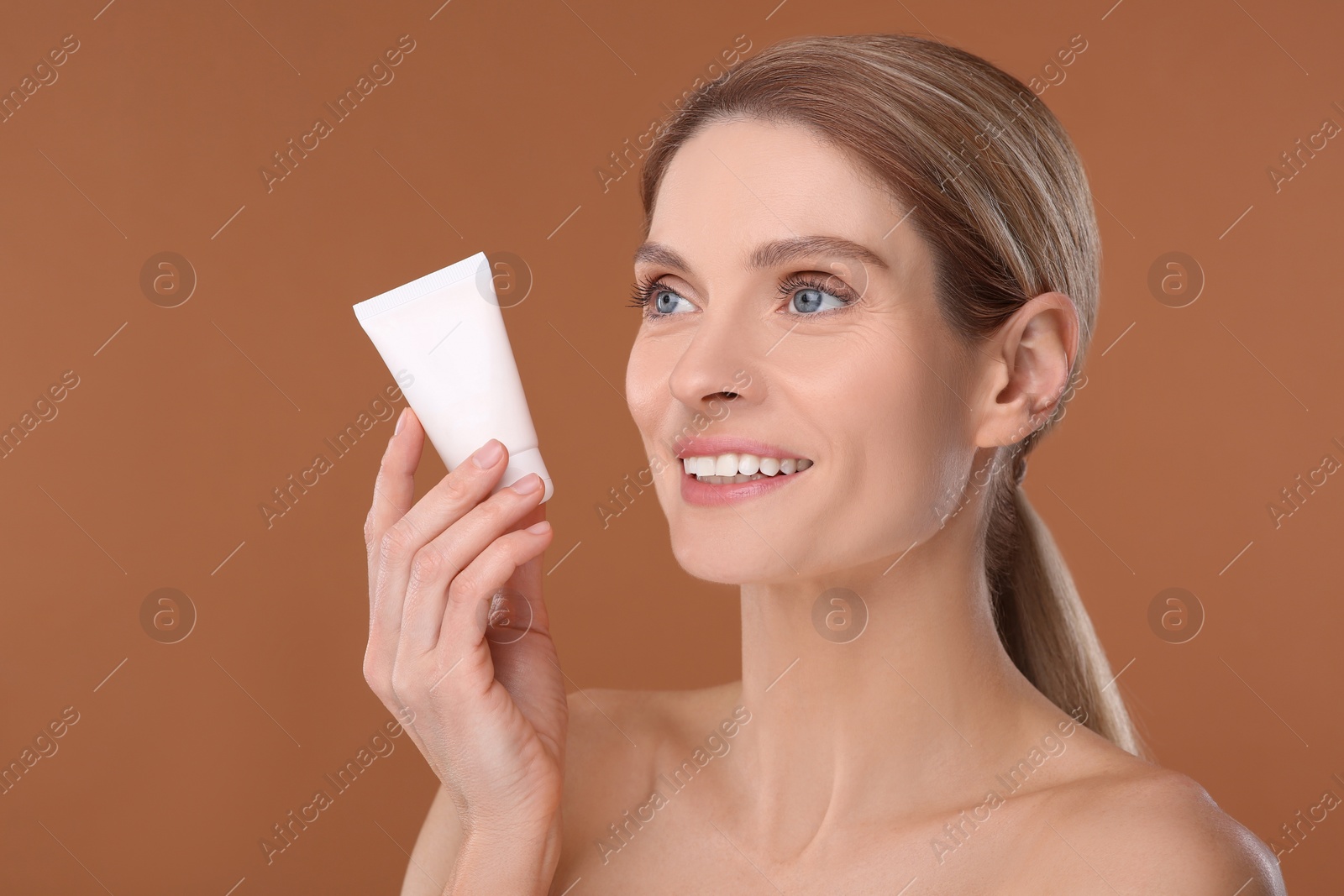 Photo of Woman holding tube of foundation on brown background