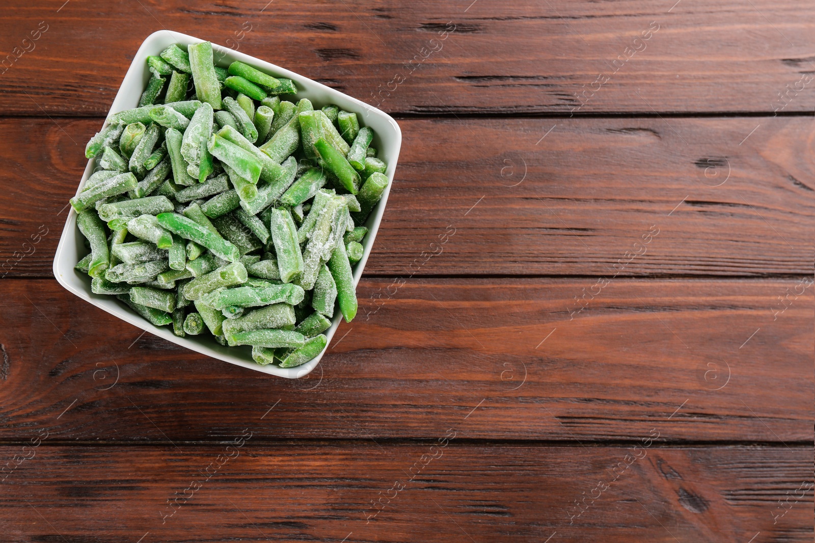 Photo of Frozen cut green beans on wooden table, top view with space for text. Vegetable preservation