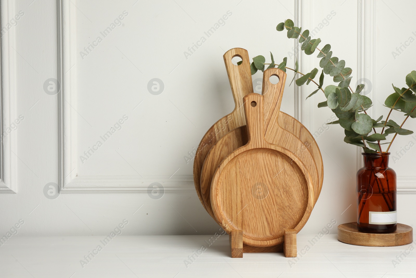 Photo of Wooden cutting boards and vase with eucalyptus branches on white table, space for text