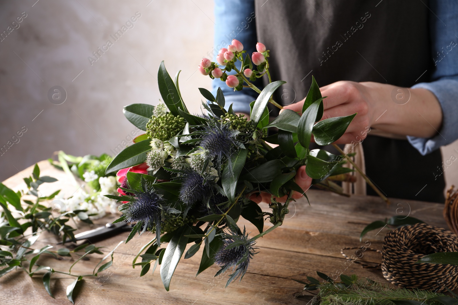 Photo of Florist making beautiful bouquet with fresh flowers at wooden table, closeup