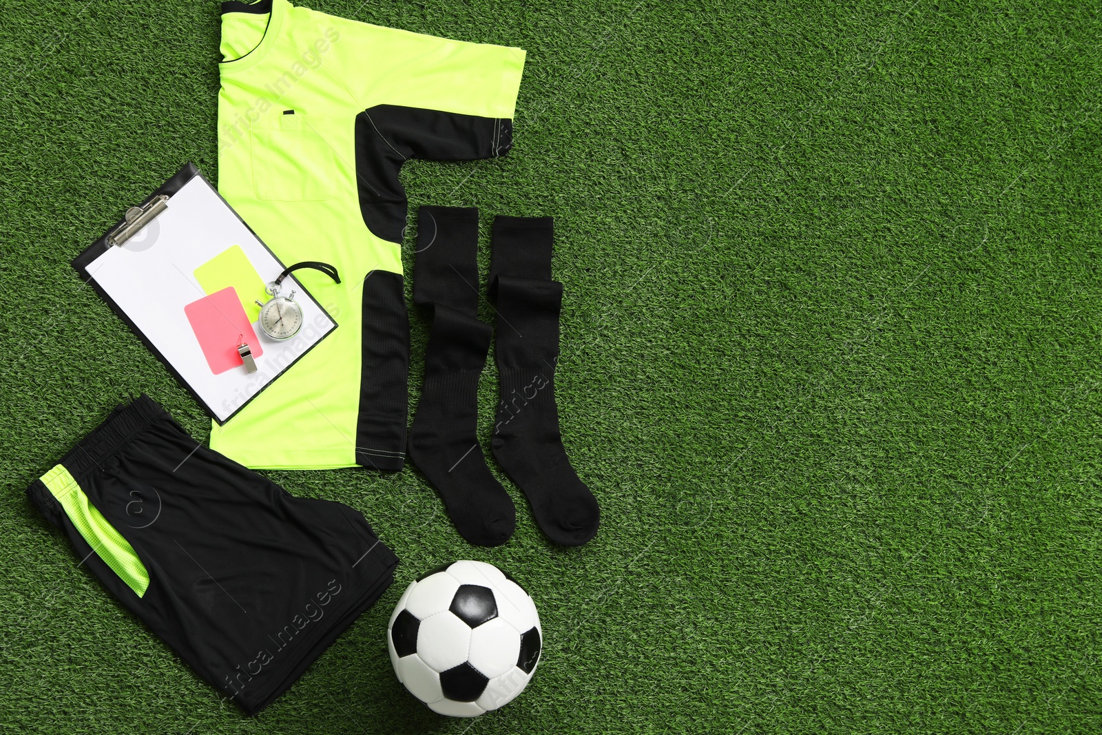 Photo of Uniform, soccer ball and other referee equipment on green grass, flat lay. Space for text