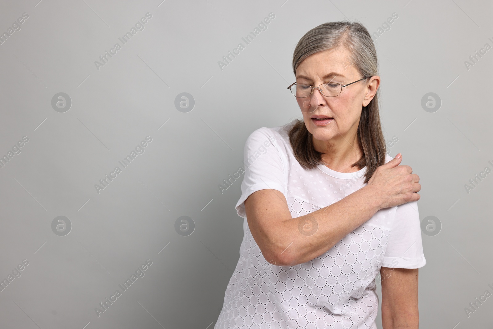 Photo of Arthritis symptoms. Woman suffering from pain in shoulder on gray background, space for text