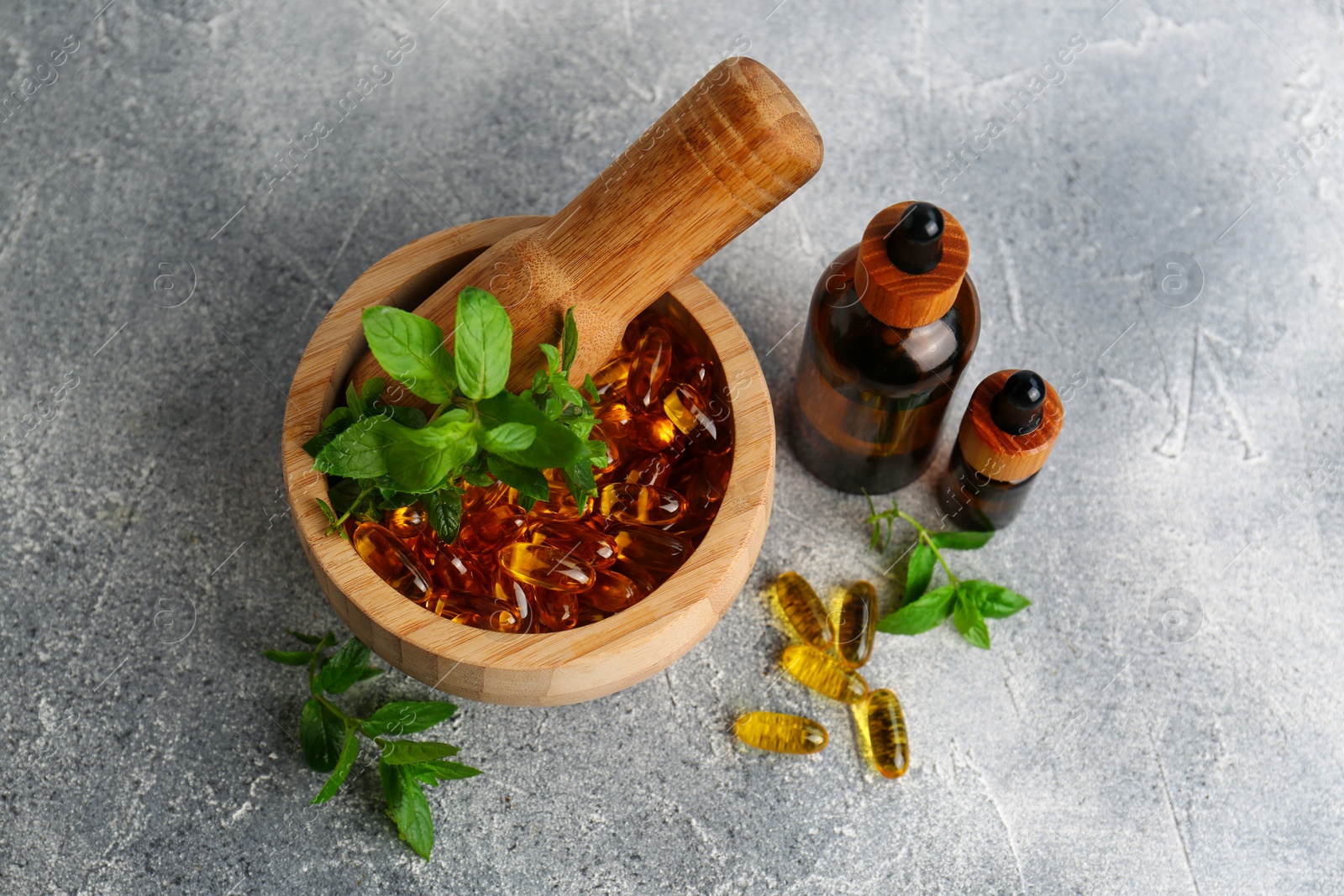 Photo of Wooden mortar with fresh green herbs, extracts and capsules on light grey table, flat lay