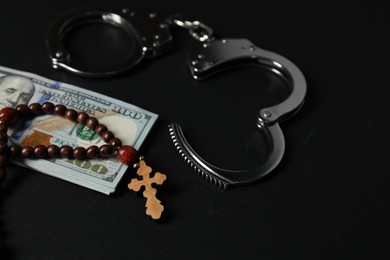 Photo of Dollars, handcuffs and prayer beads on black table