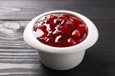 Photo of Fresh cranberry sauce in bowl on black wooden table, closeup