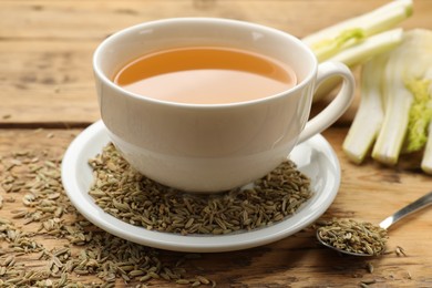 Photo of Fennel tea in cup, seeds and fresh vegetable on wooden table, closeup