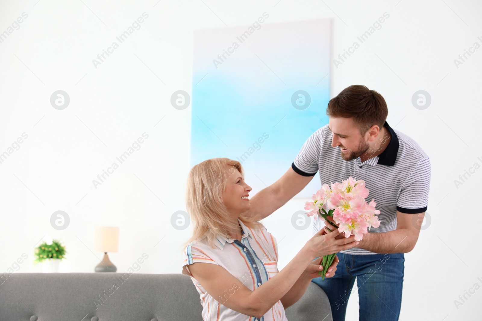 Photo of Young man congratulating his mature mom at home. Happy Mother's Day