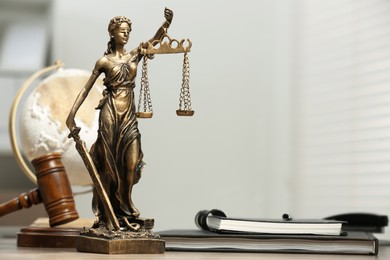 Figure of Lady Justice, gavel, globe and notebooks on table indoors, space for text. Symbol of fair treatment under law