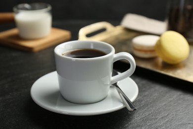 Photo of Hot coffee in cup, saucer and spoon on dark textured table, closeup