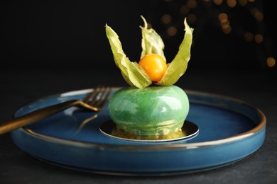 Photo of Delicious mousse cake decorated with physalis fruit on black table