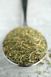 Photo of Spoon with dried dill on light grey table, closeup