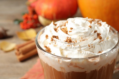 Tasty pumpkin spice latte with whipped cream on wooden table, closeup