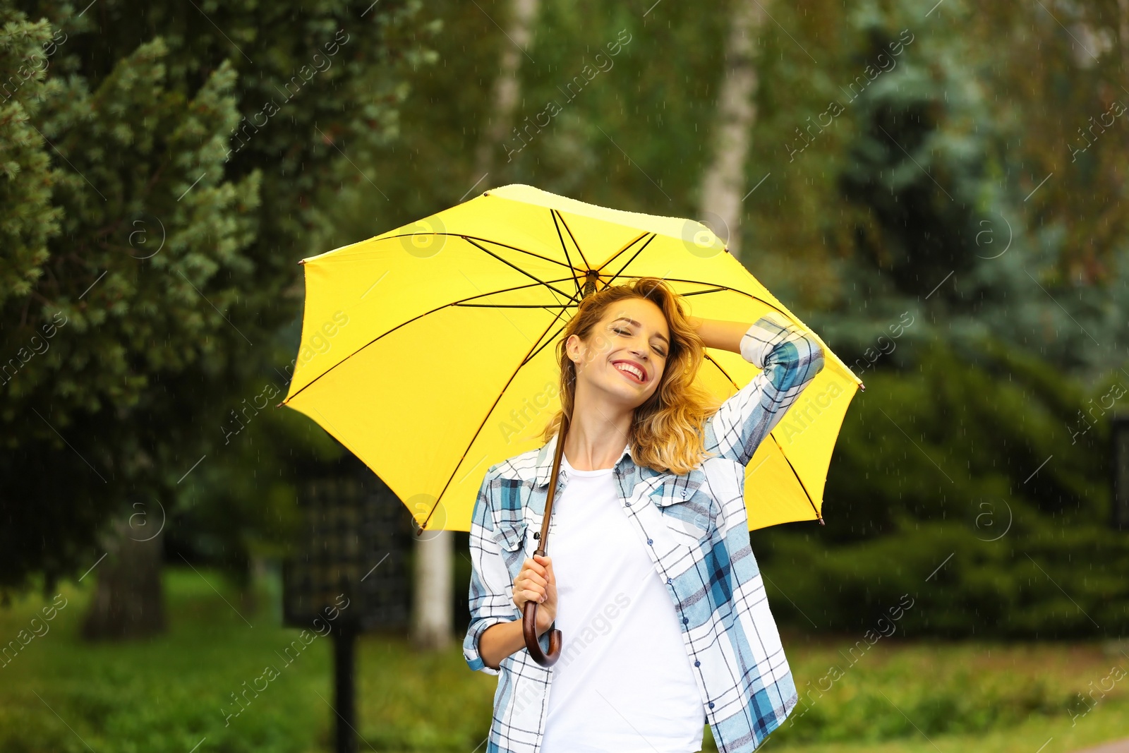 Photo of Happy young woman with umbrella under rain in park