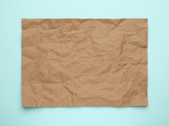 Photo of Sheet of crumpled brown paper on light blue background, top view