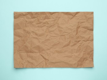 Sheet of crumpled brown paper on light blue background, top view