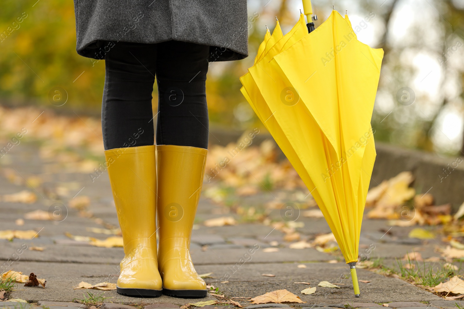 Photo of Woman with yellow umbrella and rubber boots in autumn park, closeup