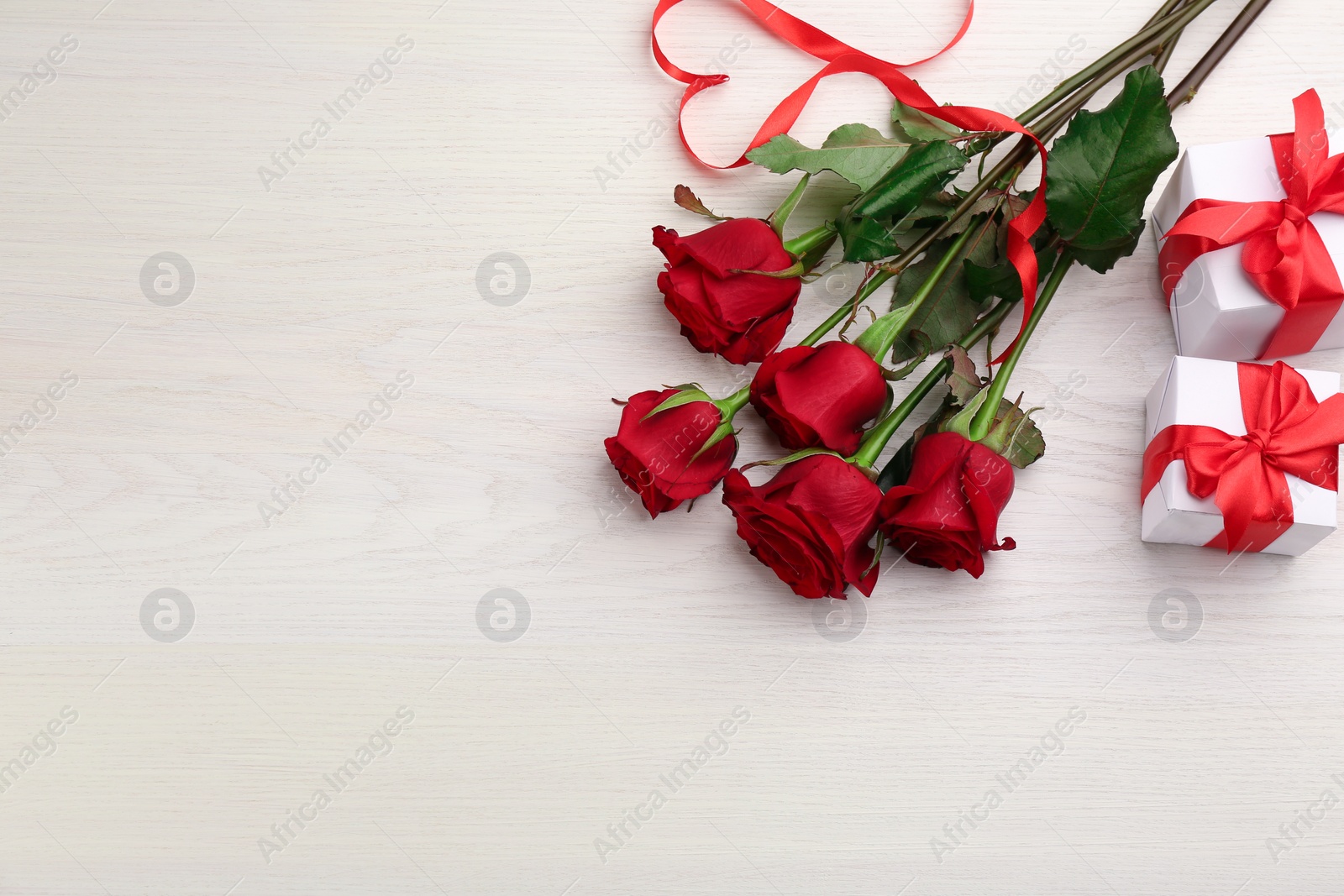 Photo of Beautiful red roses, heart shape made of ribbon and gift boxes on white wooden background, flat lay with space for text. Valentine's Day celebration