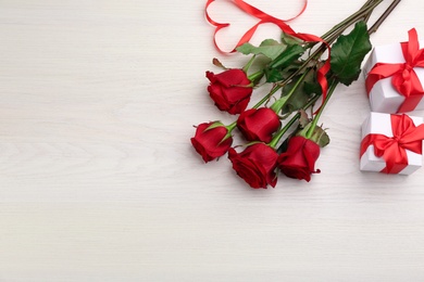 Beautiful red roses, heart shape made of ribbon and gift boxes on white wooden background, flat lay with space for text. Valentine's Day celebration