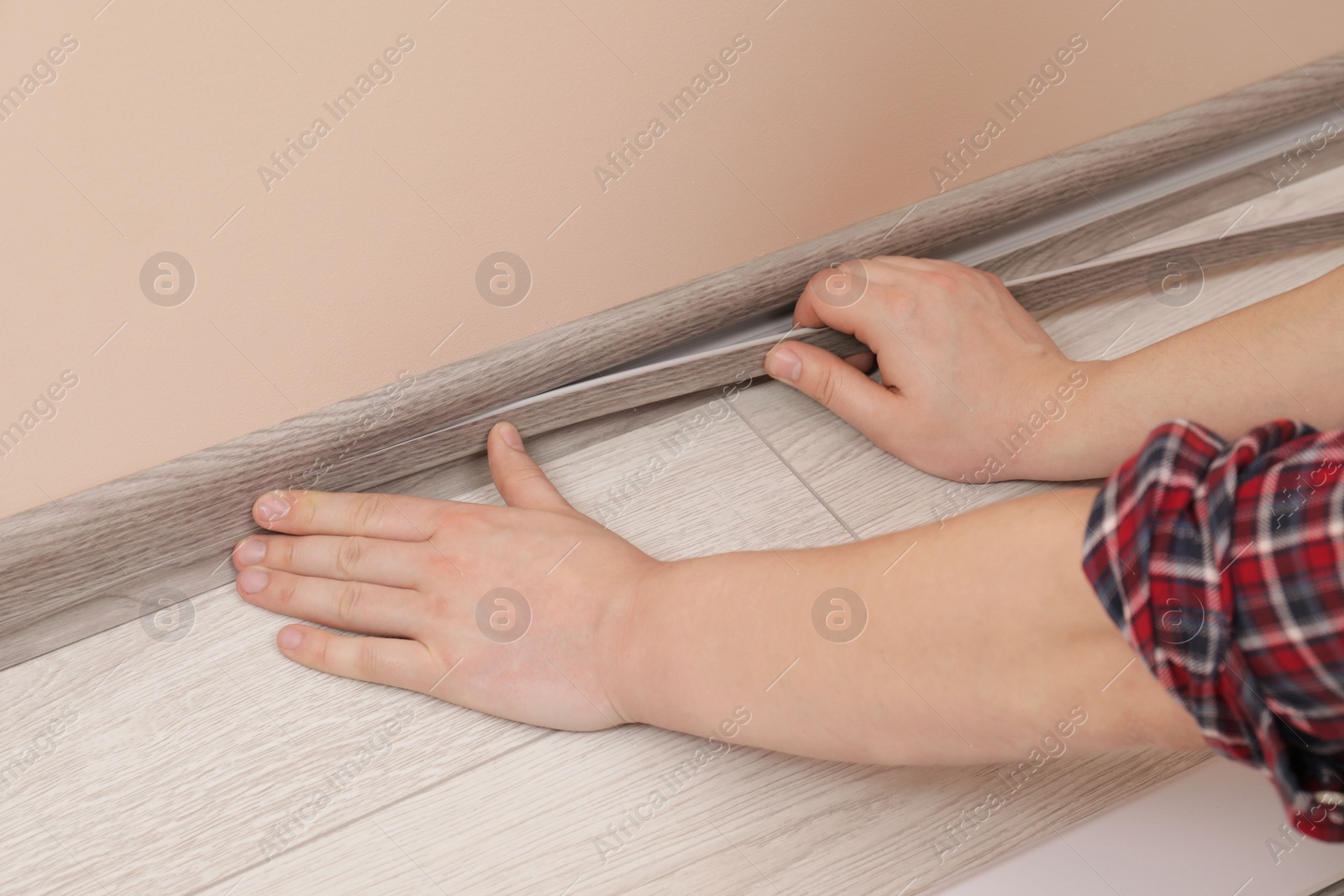 Photo of Man installing plinth on laminated floor in room, closeup