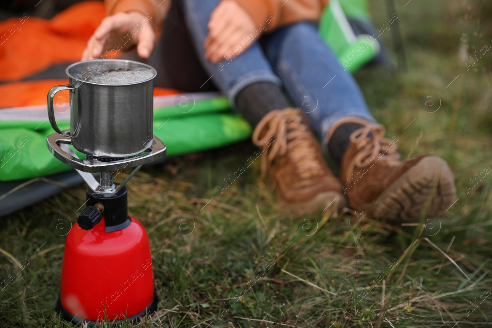 Photo of Woman taking cup off stove while sitting in camping tent outdoors, closeup