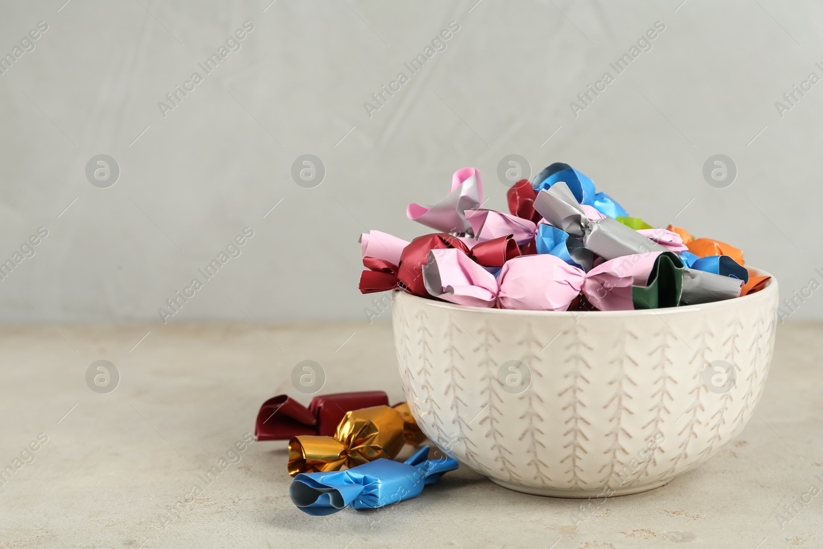 Photo of Candies in colorful wrappers on light beige table, space for text