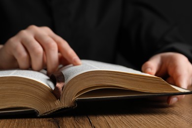 Photo of Closeup of woman reading Bible at wooden table, focus on book