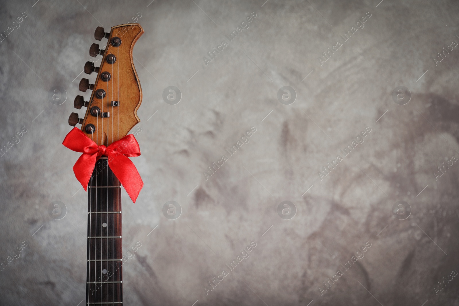 Photo of Guitar with red bow on grey background, space for text. Christmas music