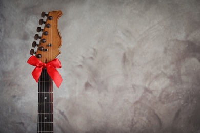 Photo of Guitar with red bow on grey background, space for text. Christmas music