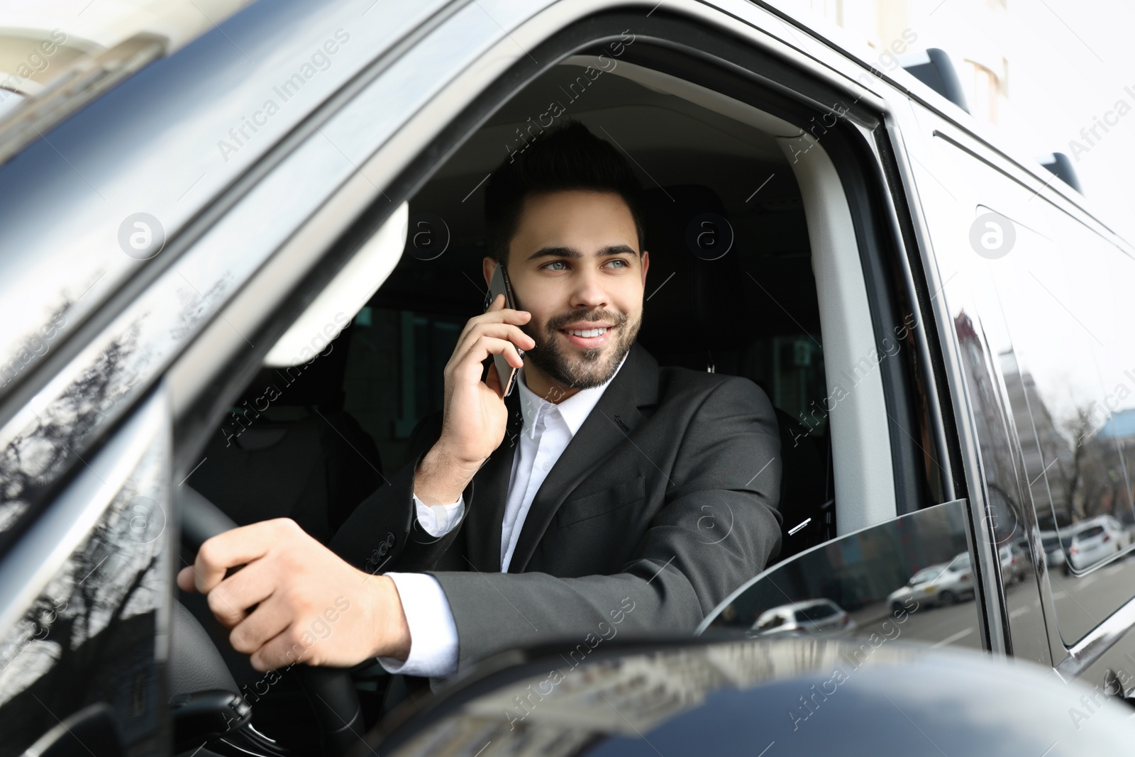 Photo of Handsome young man talking on smartphone while driving his car