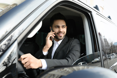 Handsome young man talking on smartphone while driving his car