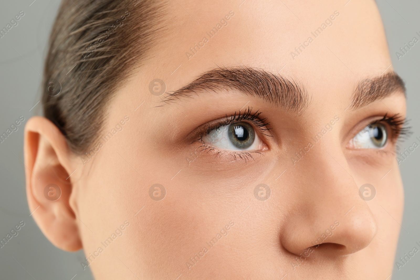 Photo of Young woman with perfect eyebrows on grey background, closeup