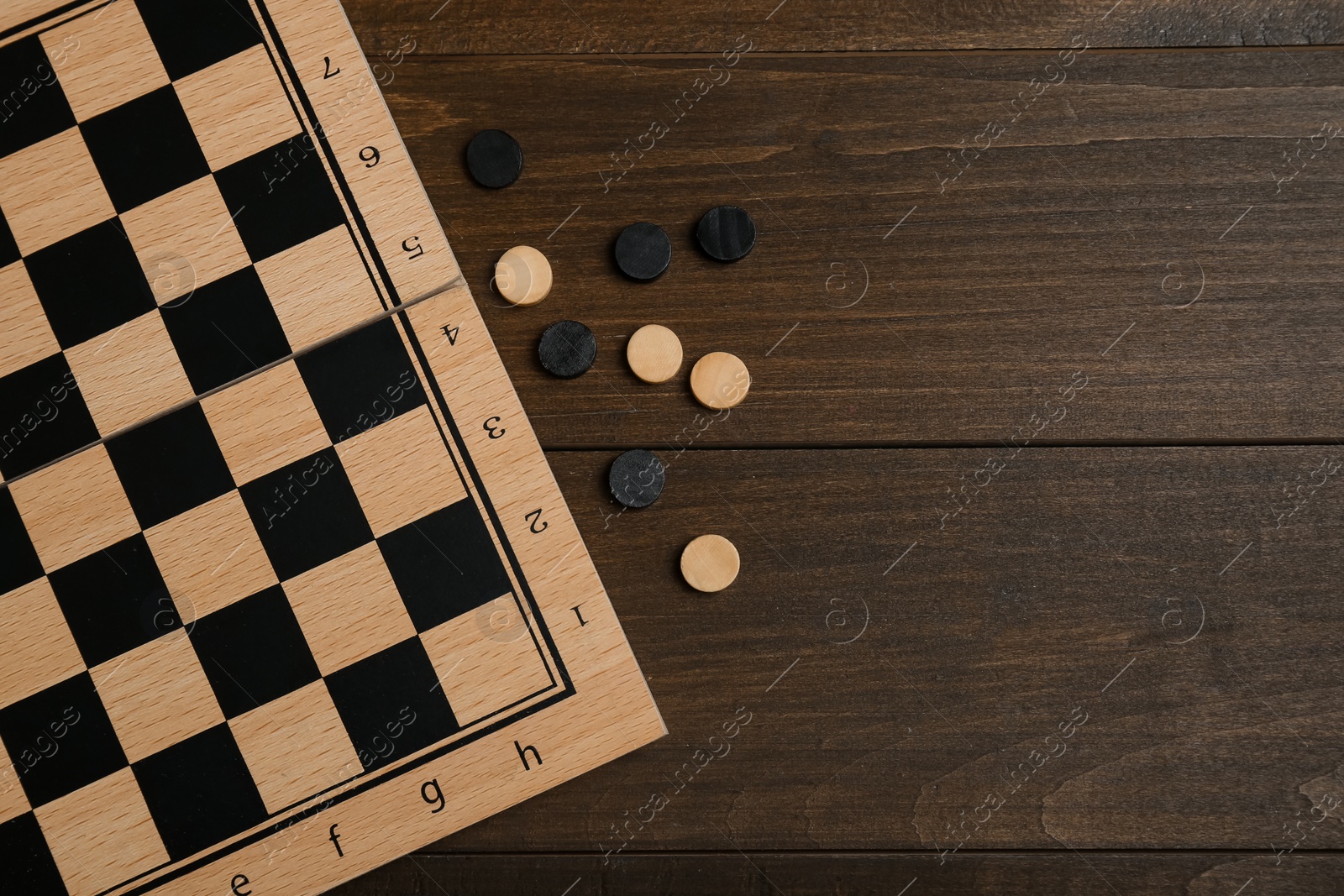 Photo of Checkerboard and game pieces on wooden table, flat lay. Space for text