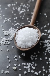 Photo of Natural salt and wooden spoon on black table