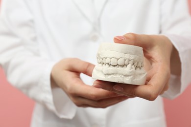 Photo of Doctor holding dental model with jaws on pink background, selective focus. Cast of teeth