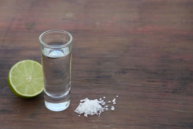 Photo of Mexican tequila shots with lime and salt on wooden table. Space for text