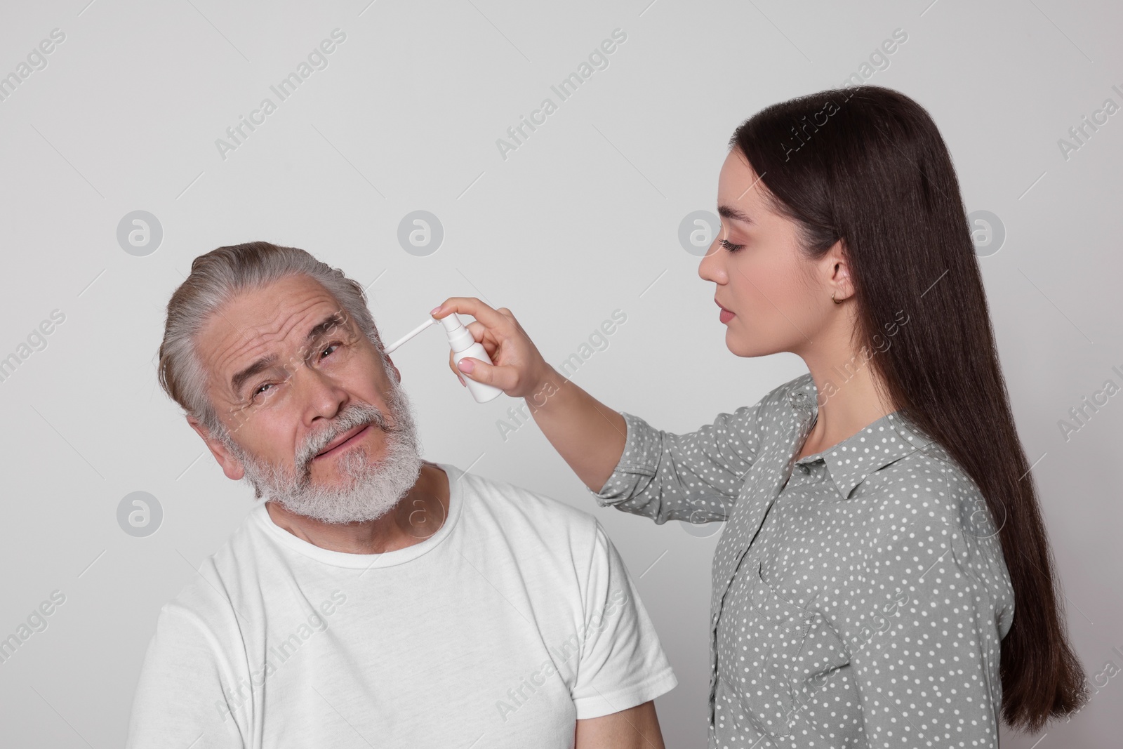 Photo of Young woman spraying medication into man's ear on white background