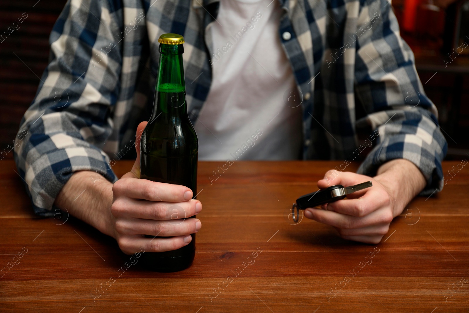 Photo of Man with bottle of beer and car keys at table, closeup. Don't drink and drive concept