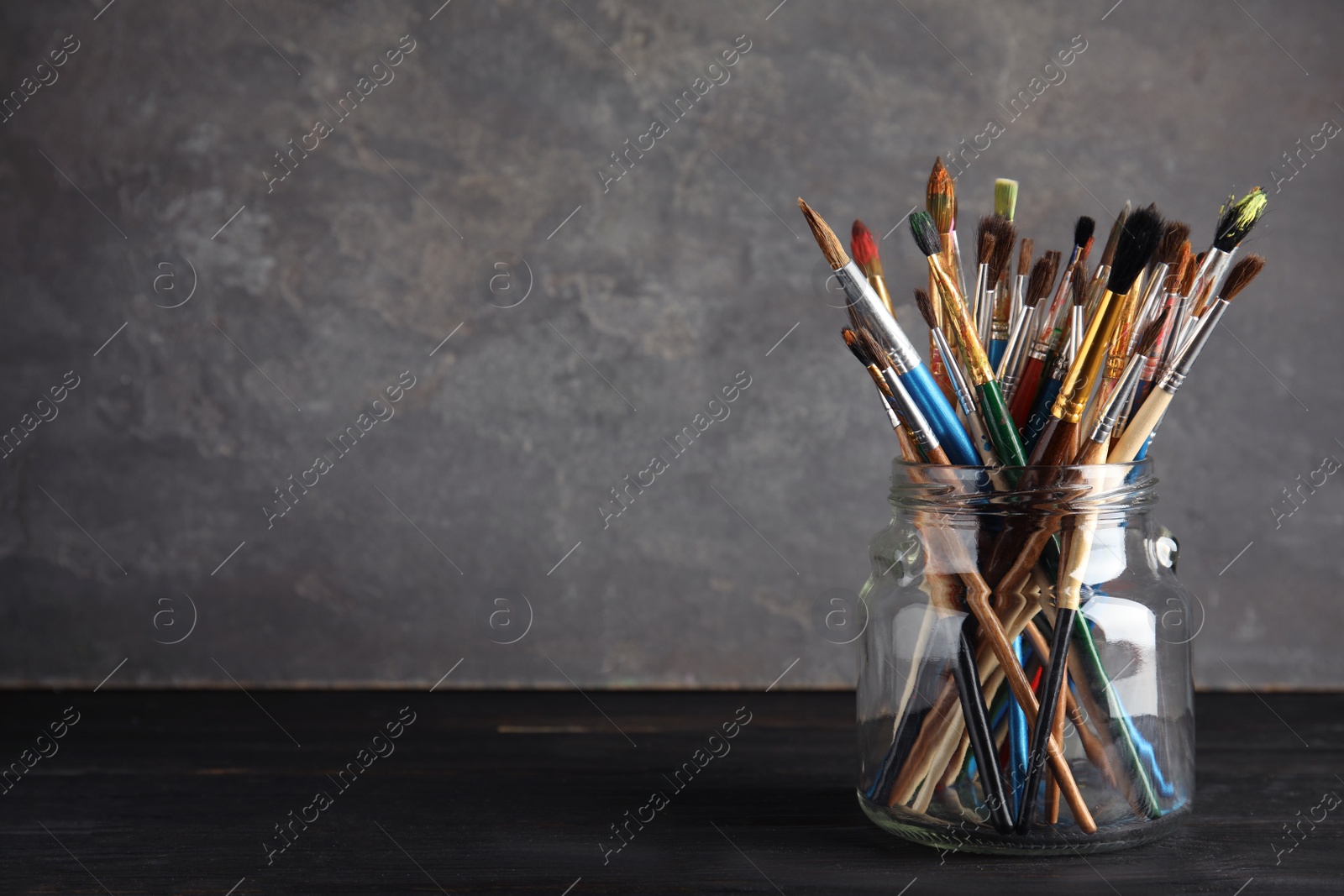 Photo of Jar with paint brushes on table against grey background. Space for text