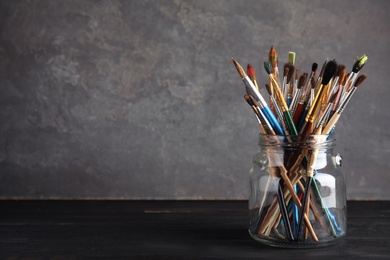 Jar with paint brushes on table against grey background. Space for text